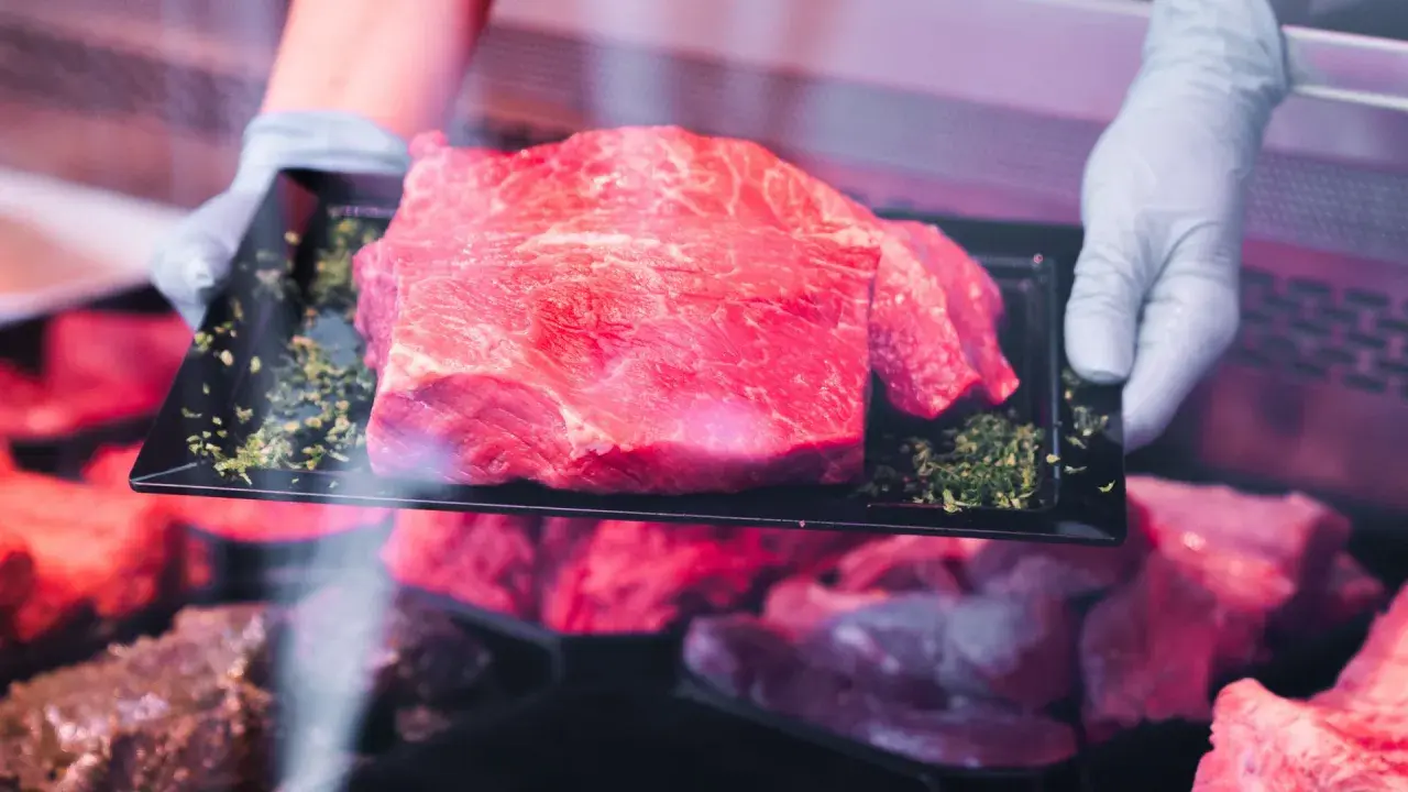 Frisch präsentiertes Rindfleisch auf einem schwarzen Teller, umgeben von Kräutern. Hoffentlich riecht das Rindfleisch nicht sauer.