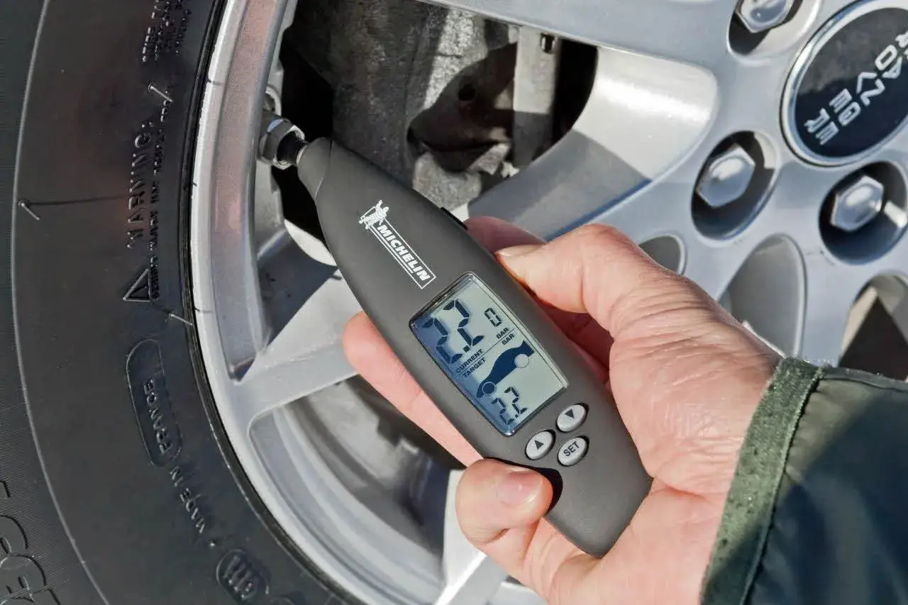 Mano usa un medidor digital Michelin para comprobar la **pegatina presión neumáticos** de un coche.