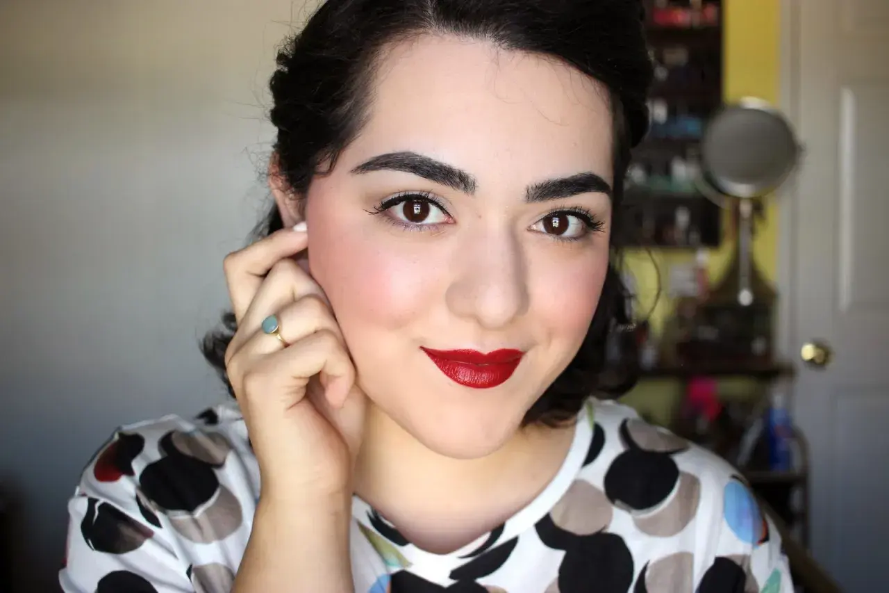 Mujer con un look de maquillaje años 40, labios rojos intensos, delineado de ojos y rubor rosado.