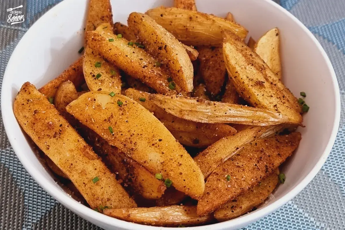 Un tazón lleno de patatas deluxe crujientes, sazonadas con especias y hierbas frescas.