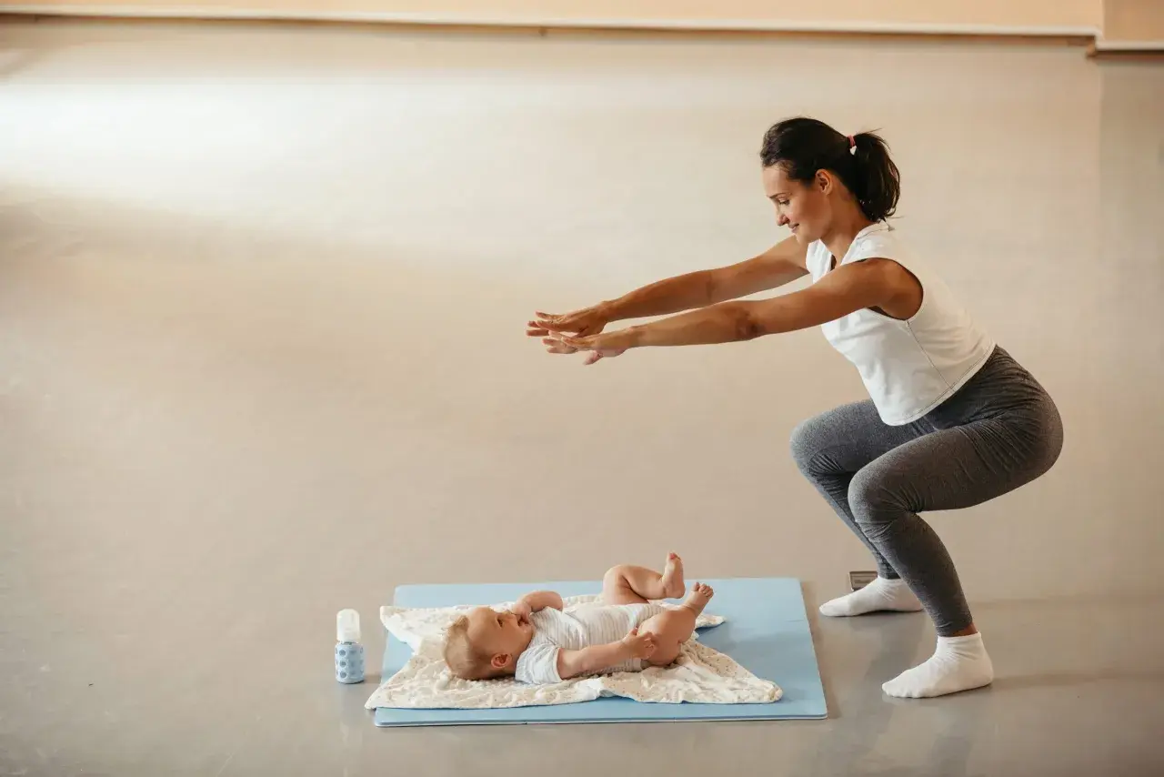 Madre haciendo sentadillas con su bebé cerca, un ejemplo de deporte postparto.