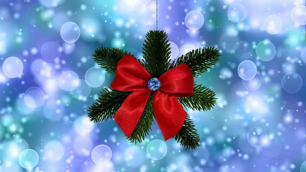 Un lazo de navidad rojo brillante adorna una rama de pino, suspendido sobre un fondo azul con luces bokeh.