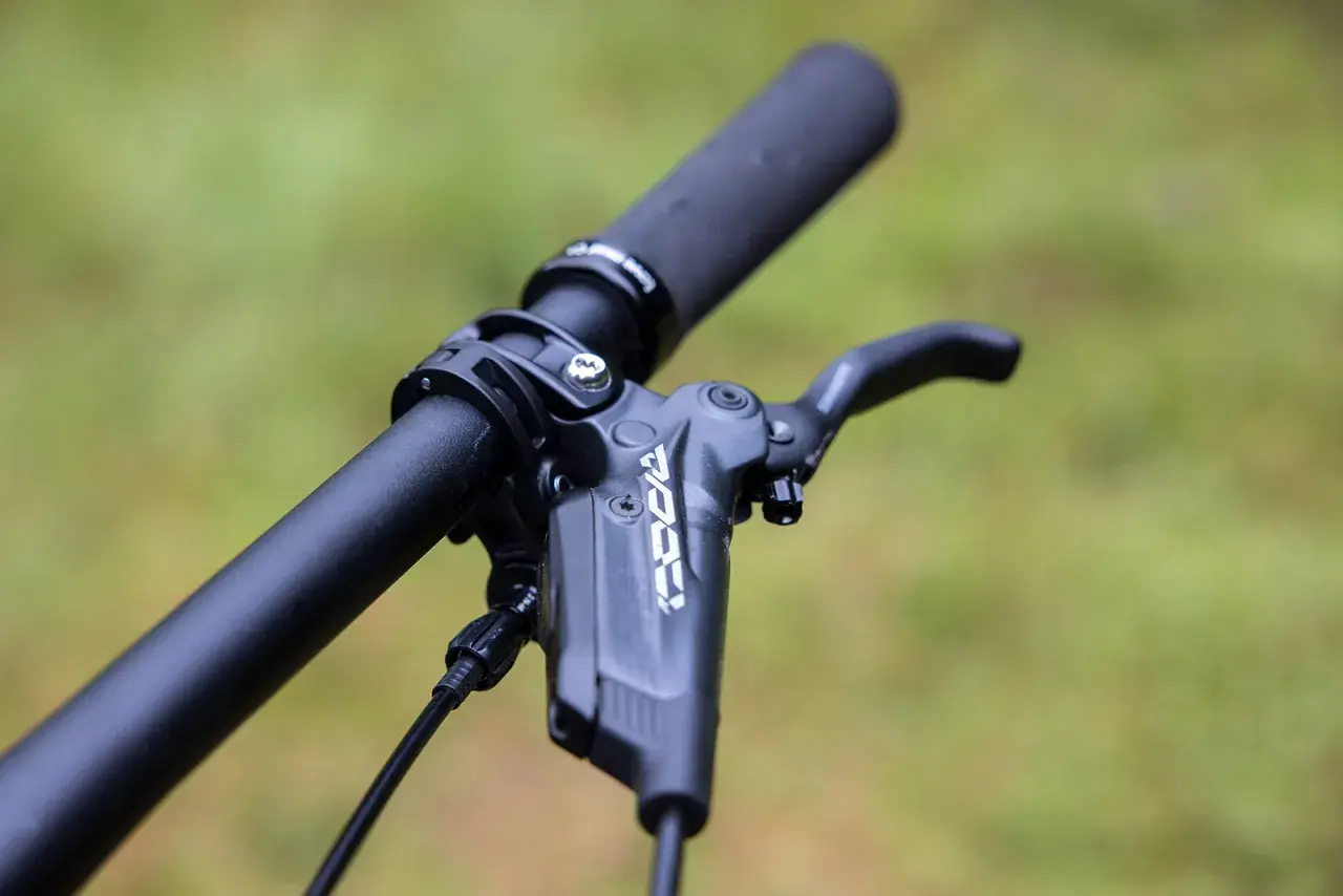 Close-up of a bicycle handlebar with a black brake lever. The lever has "KOO" branding, suggesting a brake fluid comparison.