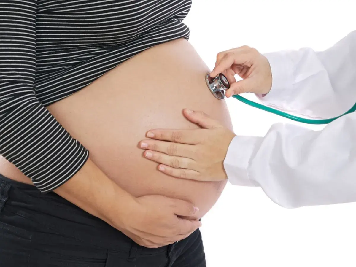 Une sage-femme utilise un stéthoscope pour le monitoring d'un ventre de femme enceinte.
