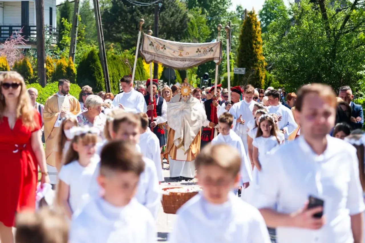 Procesja Bożego Ciała z monstrancją, księdzem i dziećmi w białych strojach.