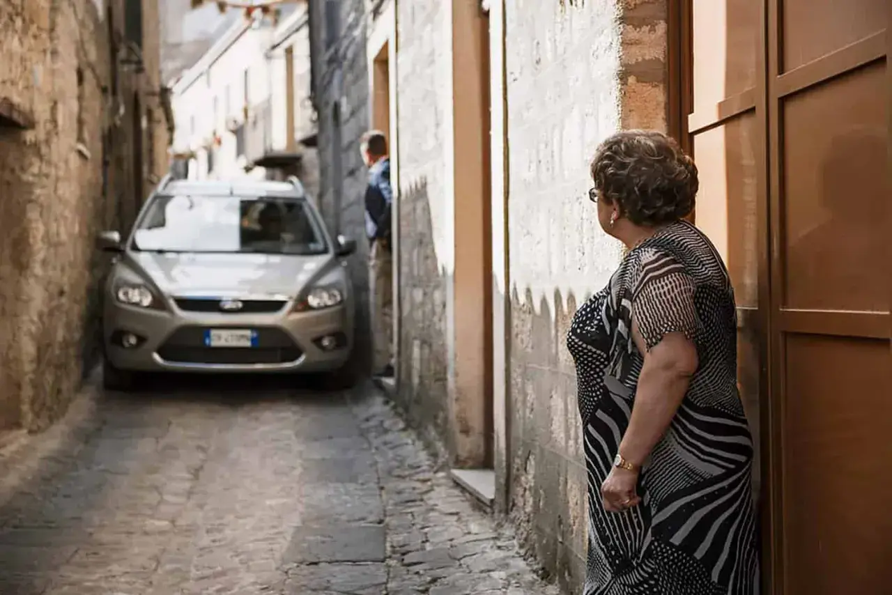 Navigating narrow Italian streets: a silver car is parked in a tight alleyway. Tips for driving in Italy for the first time include being prepared for tight squeezes.