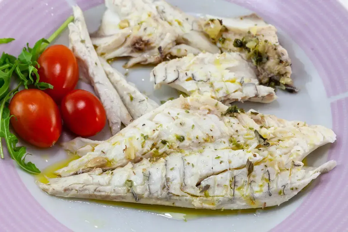 Delizioso branzino in padella, cotto alla perfezione e condito con erbe aromatiche. Servito con pomodorini freschi e rucola.