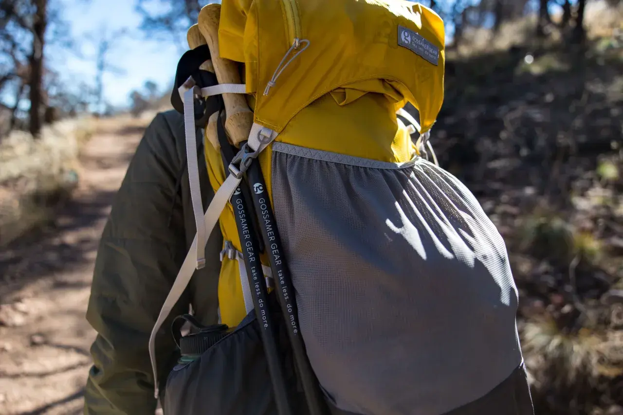 Kijki trekkingowe przymocowane do żółtego plecaka Gossamer Gear. Paski i siatkowa kieszeń pomagają w transporcie.