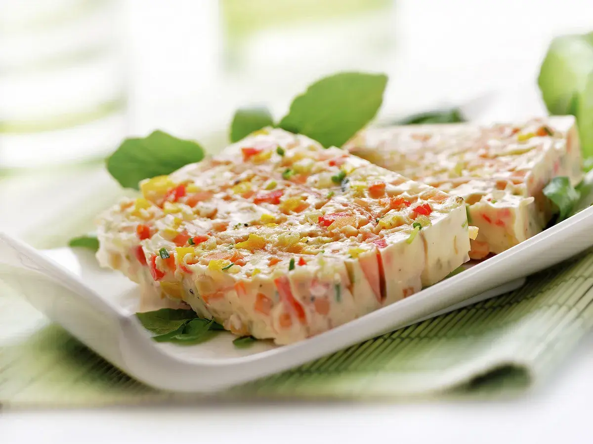 Tranches de terrine de légumes colorée, garnie de feuilles vertes, sur une assiette blanche.