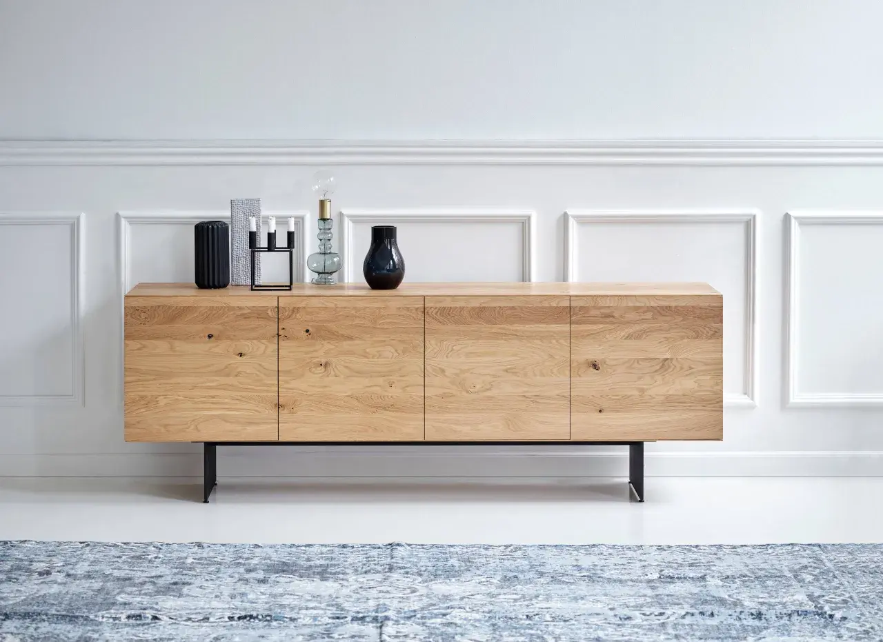 Ett stilrent sideboard i ljust trä med svarta ben, dekorerat med vaser och ljusstakar.