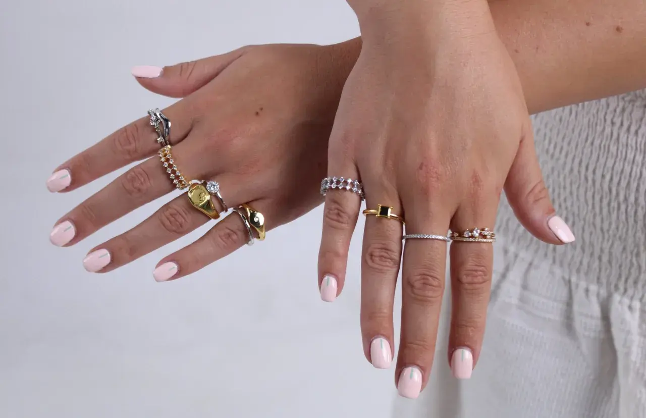 Manos con uñas rosa pálido y anillos de plata y oro. Un anillo dorado tiene un sello, otro un diamante. ¿Qué significa 925 en oro?