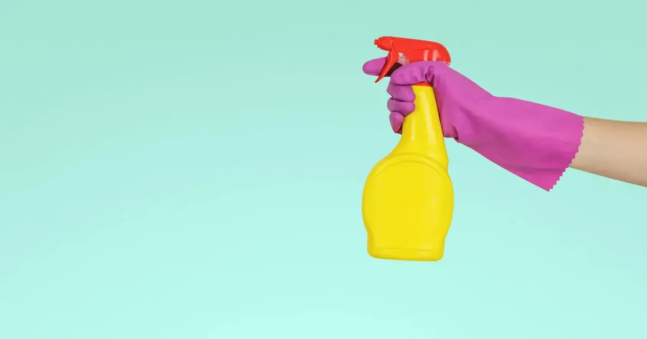 En hand i lila handske håller en gul sprayflaska med röd spraymunstycke, redo för en snabb dry clean.