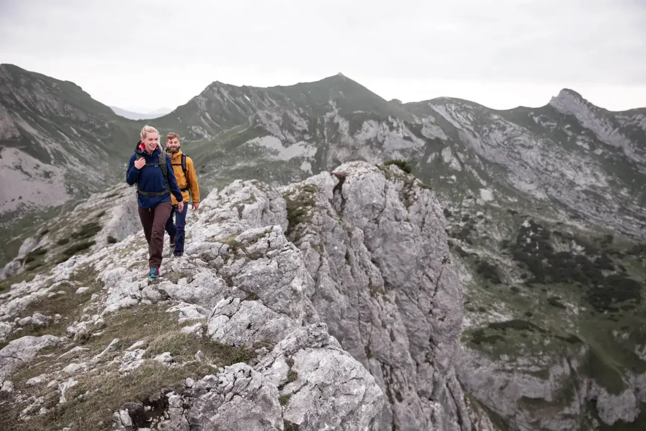 Zwei Wanderer genießen eine 5-tägige Tour durch die Alpen. Sie gehen auf einem felsigen Grat mit beeindruckender Bergkulisse.