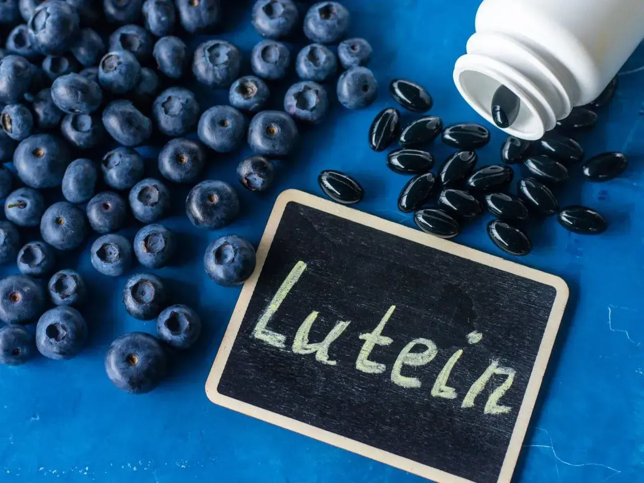 Jagody i kapsułki suplementu diety z napisem "Luteina" na tabliczce. Luteina na oczy wspiera zdrowie wzroku.