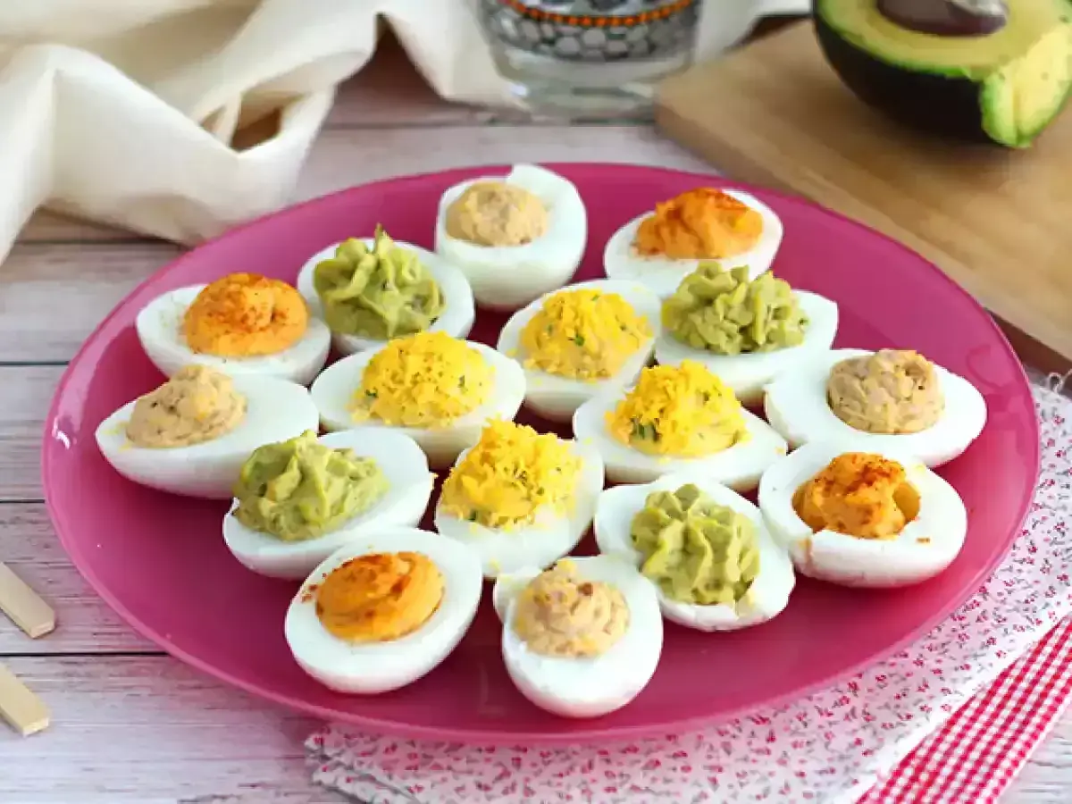 Assortiment d'œufs mimosa colorés sur une assiette rose. Des garnitures vertes, jaunes et orangées apportent une touche festive.