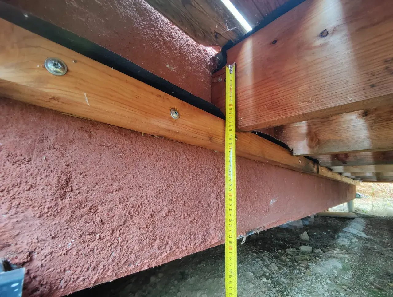 Mesure de la hauteur d'une poutre en bois extérieur, avec un revêtement rouge pour sa protection.