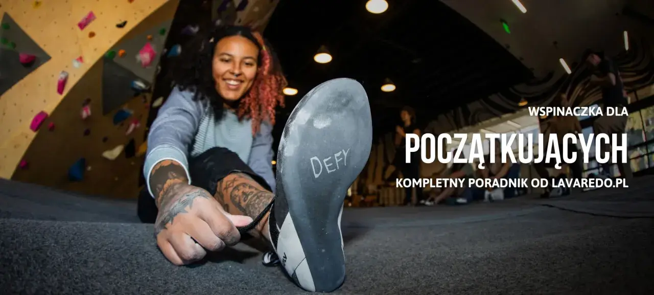 Uśmiechnięta kobieta zakłada buty do wspinaczki na ściance. Dowiedz się, bouldering co to jest i jak zacząć.