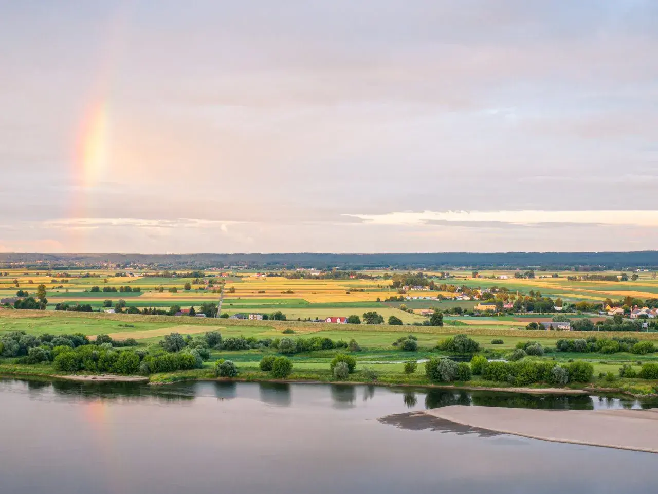 Krajobraz Kociewia nad rzeką, pola uprawne, domy i tęcza na niebie.