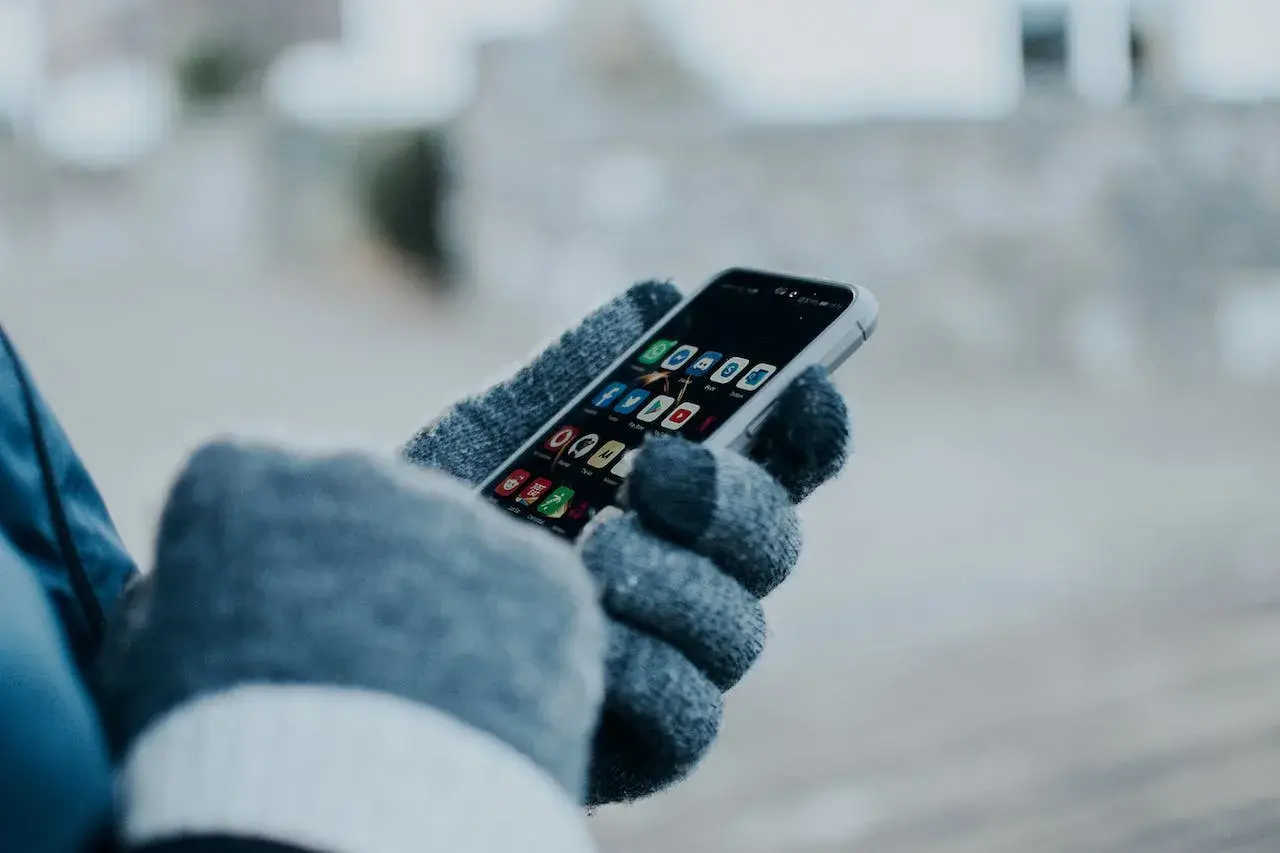Ręka w rękawiczce trzyma smartfon z ikonami aplikacji. Chcesz wiedzieć, jak sprawdzić czy ktoś jest aktywny na Facebooku?