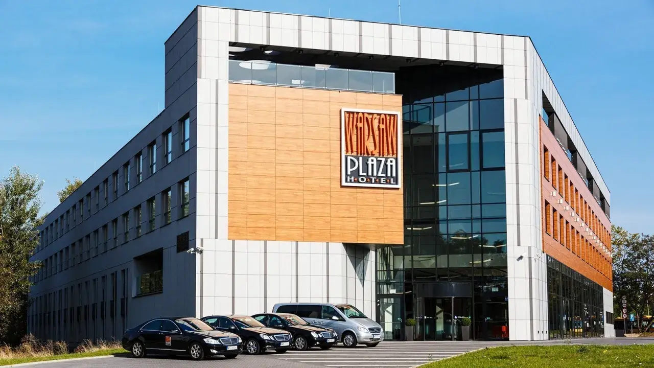 Warsaw Plaza Hotel z nowoczesną fasadą i zaparkowanymi samochodami.