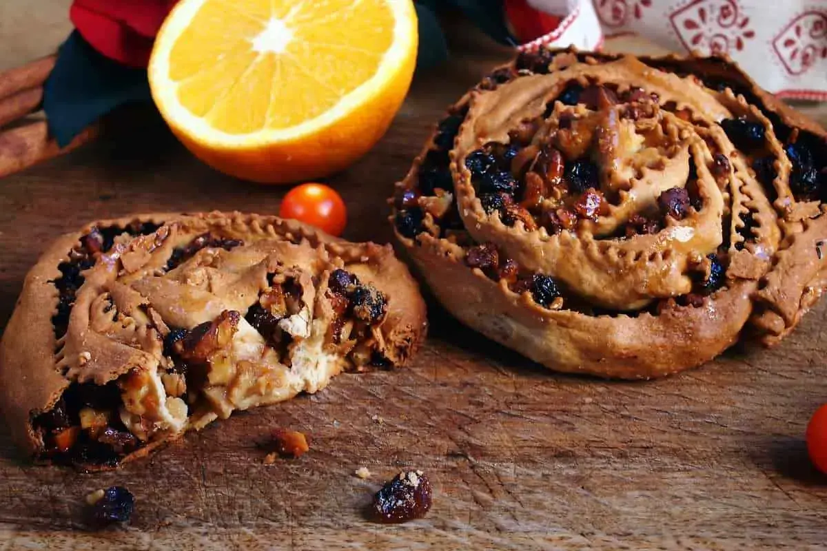 Due pitte nchiuse calabresi, dolci tradizionali con uvetta e noci, su un tagliere di legno con arancia e pomodorini.