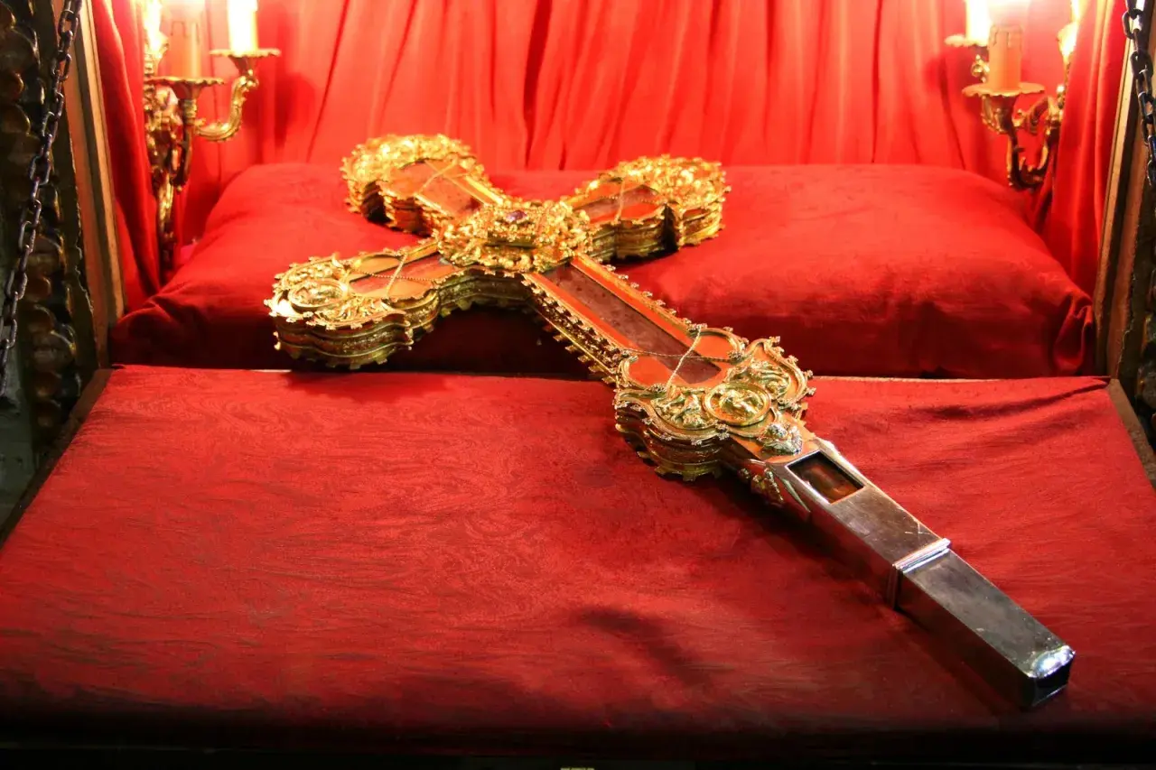 Cruz de Caravaca dorada y enjoyada, expuesta sobre terciopelo rojo en el monasterio de Santo Toribio de Liébana.
