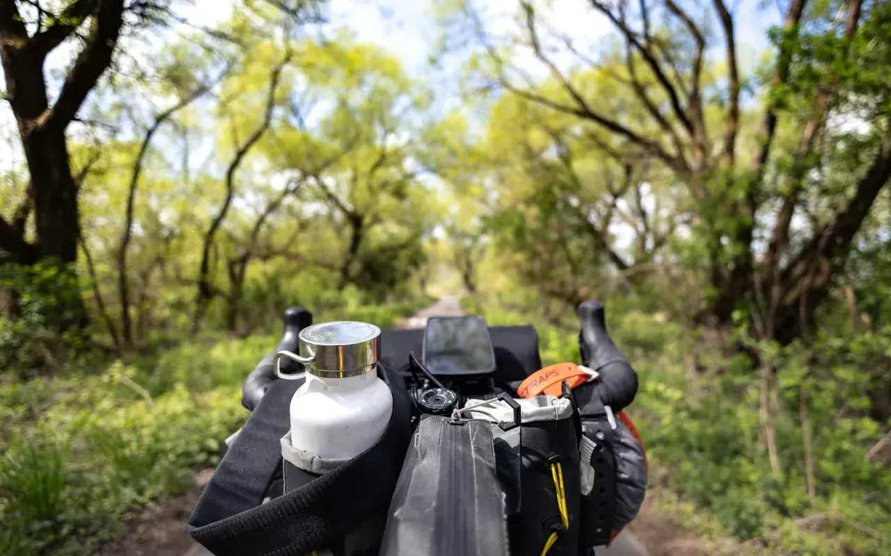 Widok z kierownicy roweru podczas bikepacking gravel. Biała butelka, nawigacja i torba podsiodłowa gotowe na przygodę.