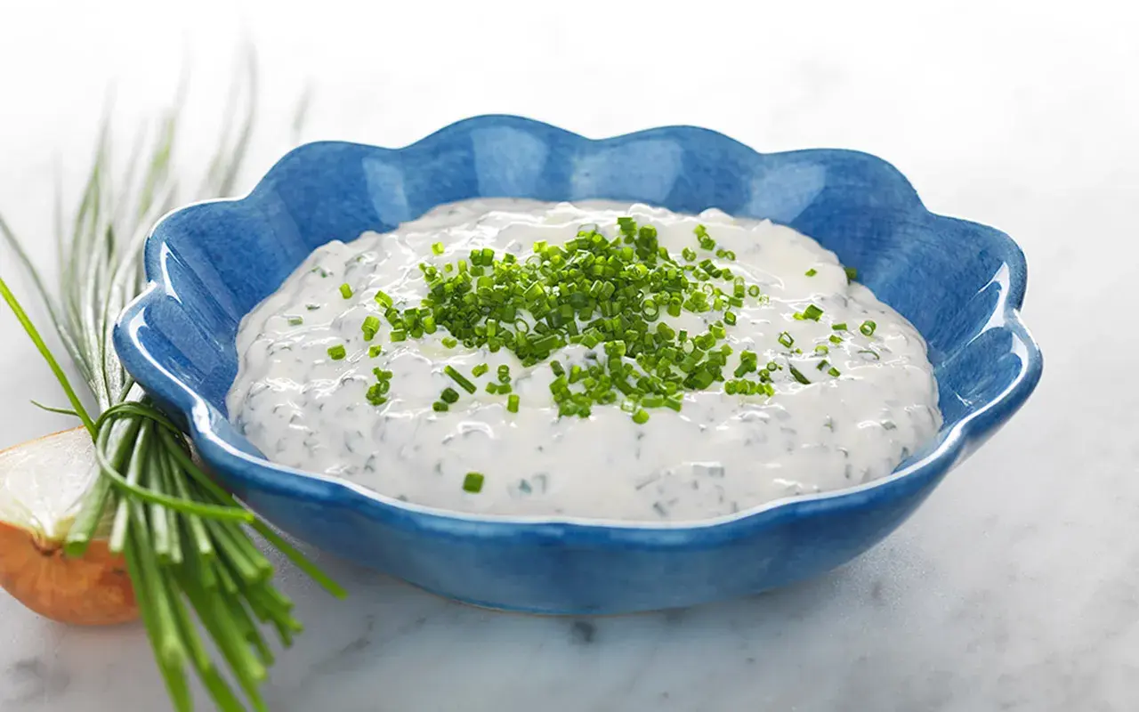Kall sås till paj, en krämig gräddfilssås med gräslök, serverad i en blå skål.