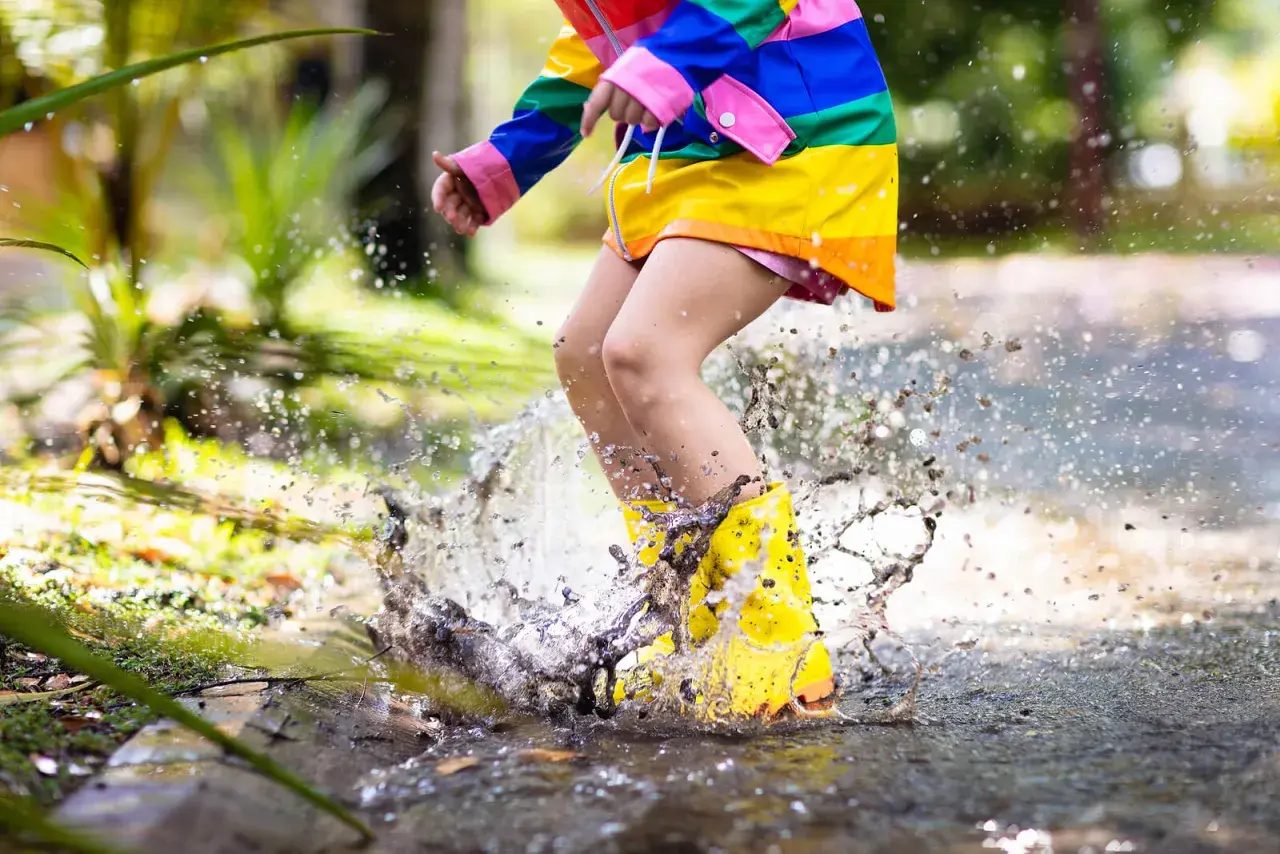 Bambino con stivali gialli salta in una pozzanghera, creando spruzzi d'acqua. Ecco perché i bambini si sdraiano per terra: per godersi il gioco!
