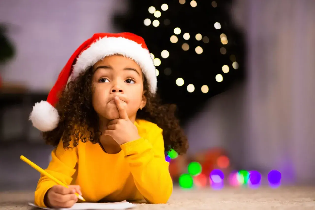 Ein kleines Mädchen mit Nikolausmütze denkt nach, während es am 6. Dezember ein Nikolausgedicht schreibt.