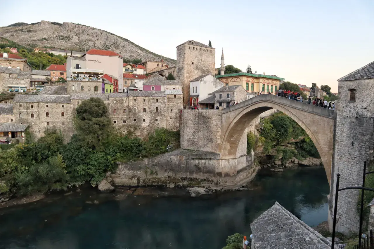 Stari Most, en ikonisk stenbro i Mostar, sträcker sig över en turkos flod. Gamla stenbyggnader och en moské omger den.