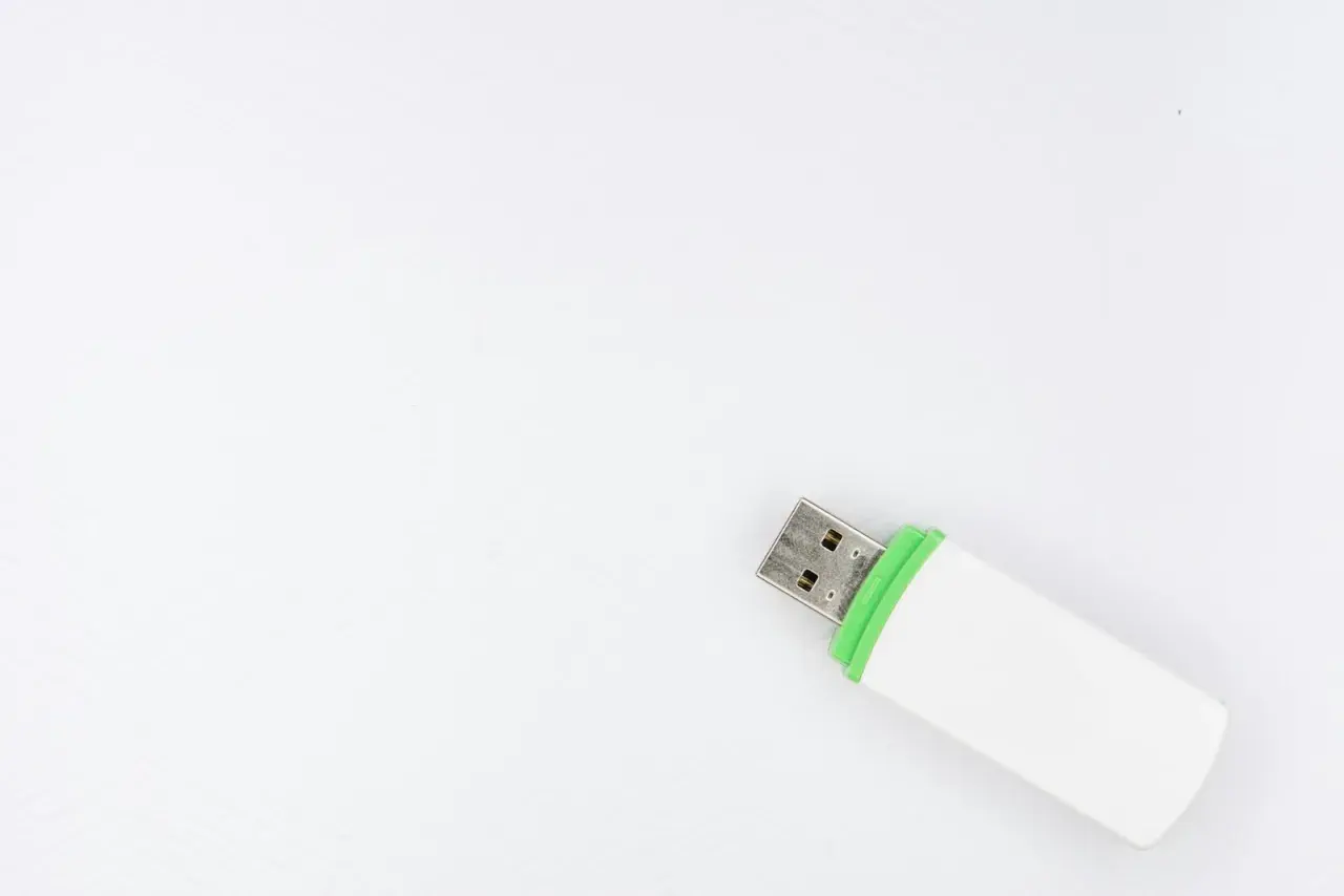 Biały pendrive z zieloną opaską, gotowy do podłączenia. Ten woe usb pomieści Twoje dane.