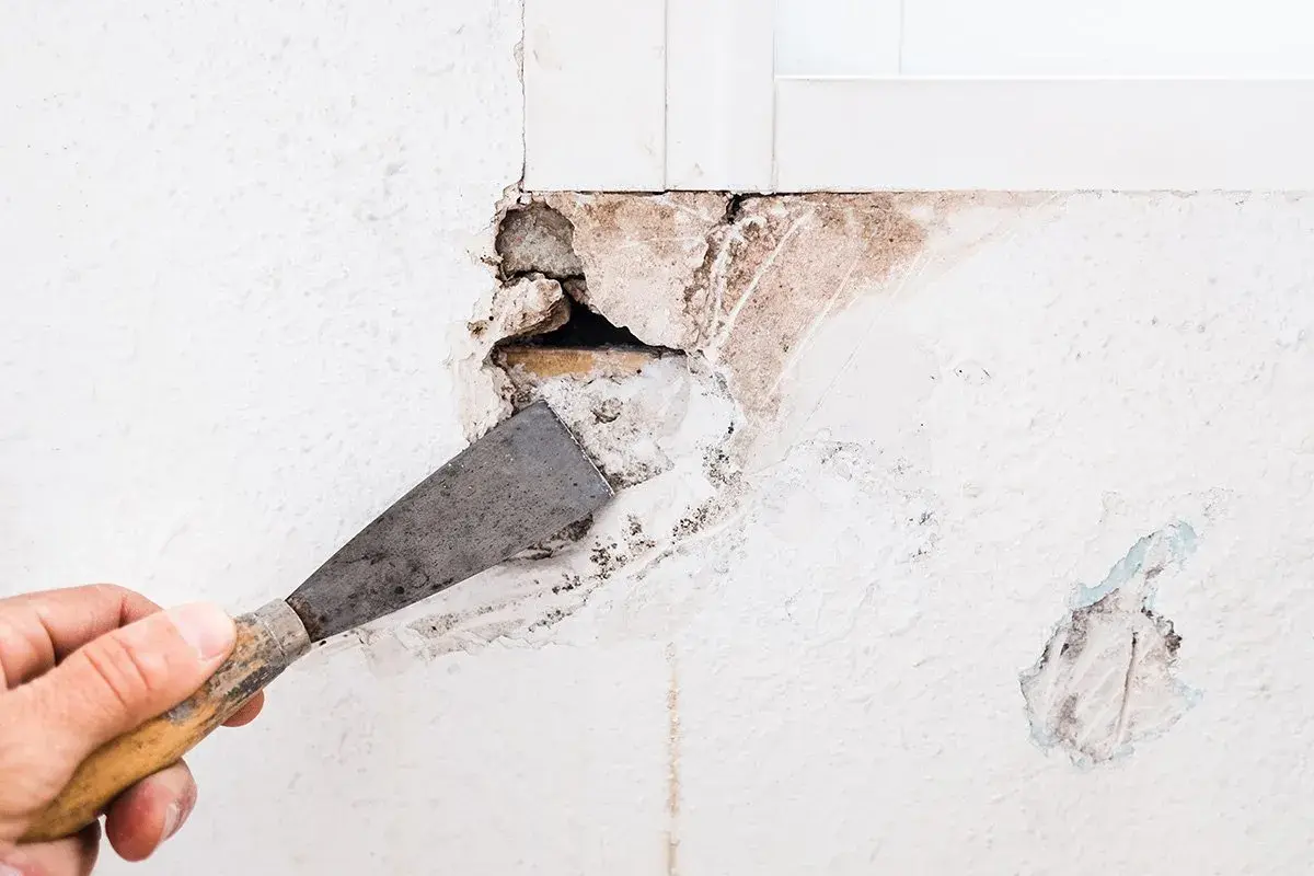 Mano con spatola che prepara un grosso buco nel muro per come riempire il muro danneggiato.