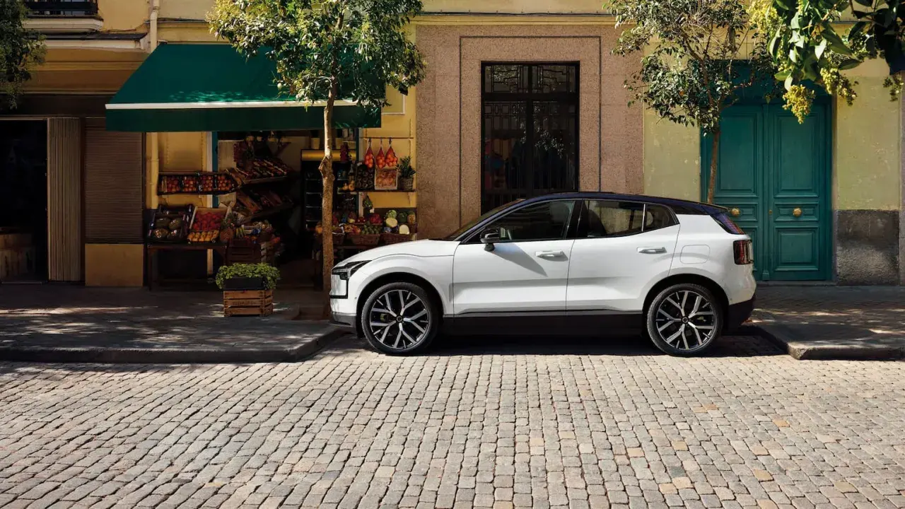 Vit Volvo parkerad på kullerstensgata framför en färggrann fasad. Upptäck olika volvo utrustningsnivåer för din nästa bil.
