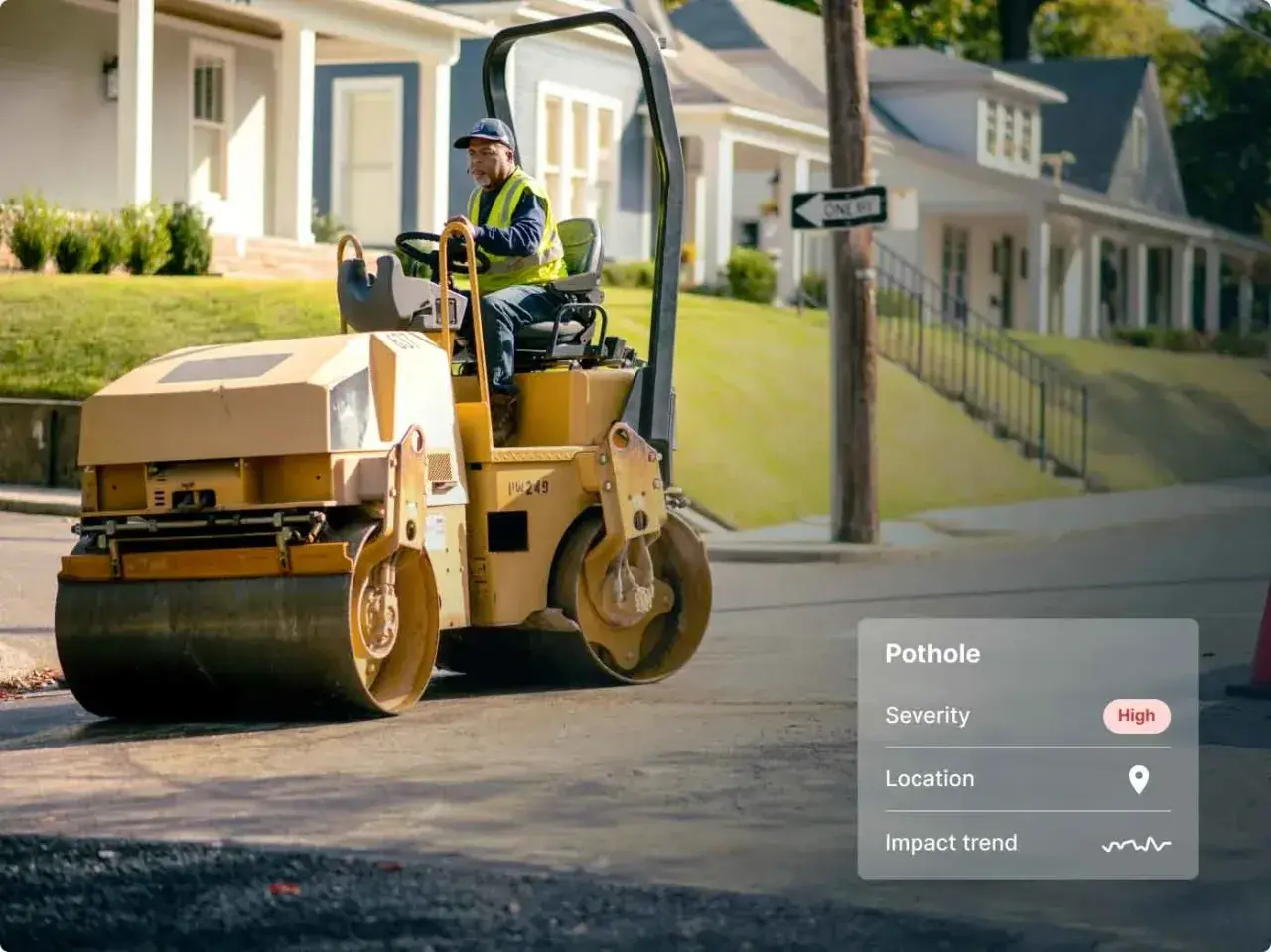 A worker operates a steamroller, ready to be a change agent and fix the high-severity pothole on this street.