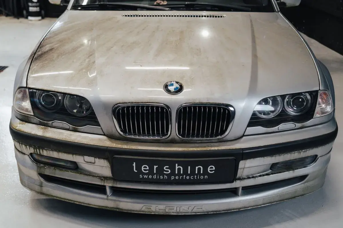 En smutsig silverfärgad BMW med synliga fläckar på huven och stötfångaren. Dags att avfetta bilen för att få fram dess glans.