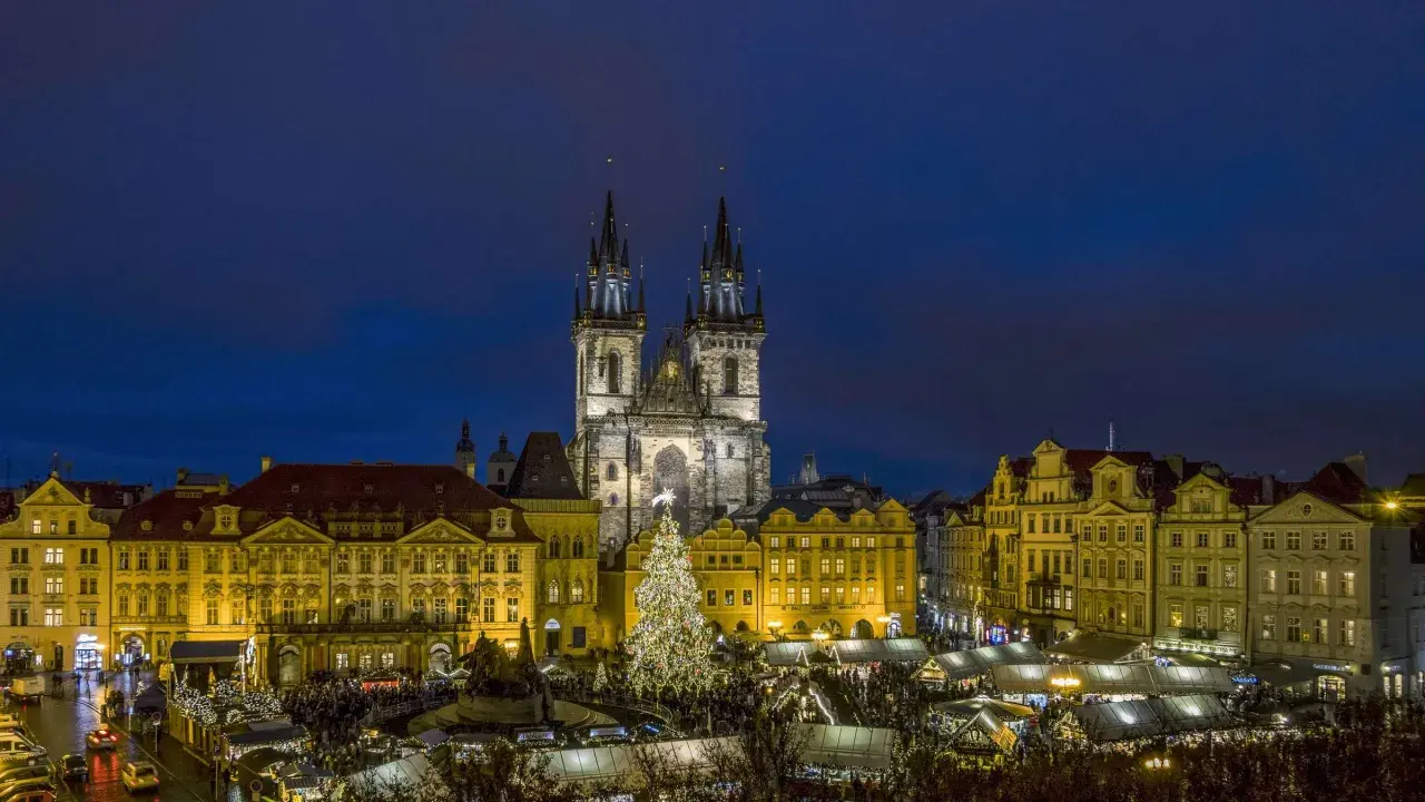 Prag im Winter: Der beleuchtete Weihnachtsbaum auf dem Altstädter Ring, umgeben von Ständen und der Teynkirche, erstrahlt in der Dämmerung.