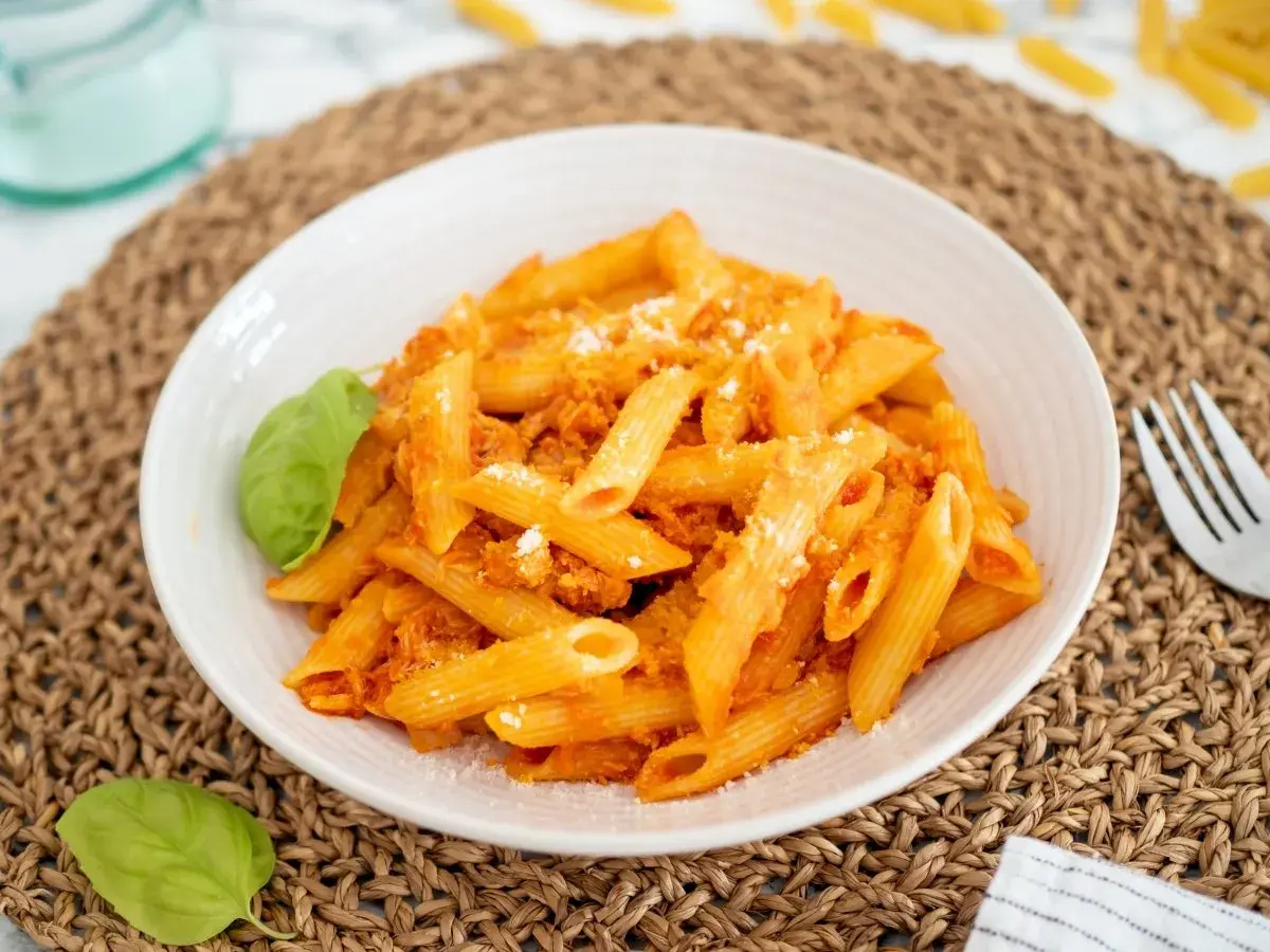 Un plato de macarrones con atún, cubiertos con salsa de tomate y queso rallado, adornado con hojas de albahaca fresca.