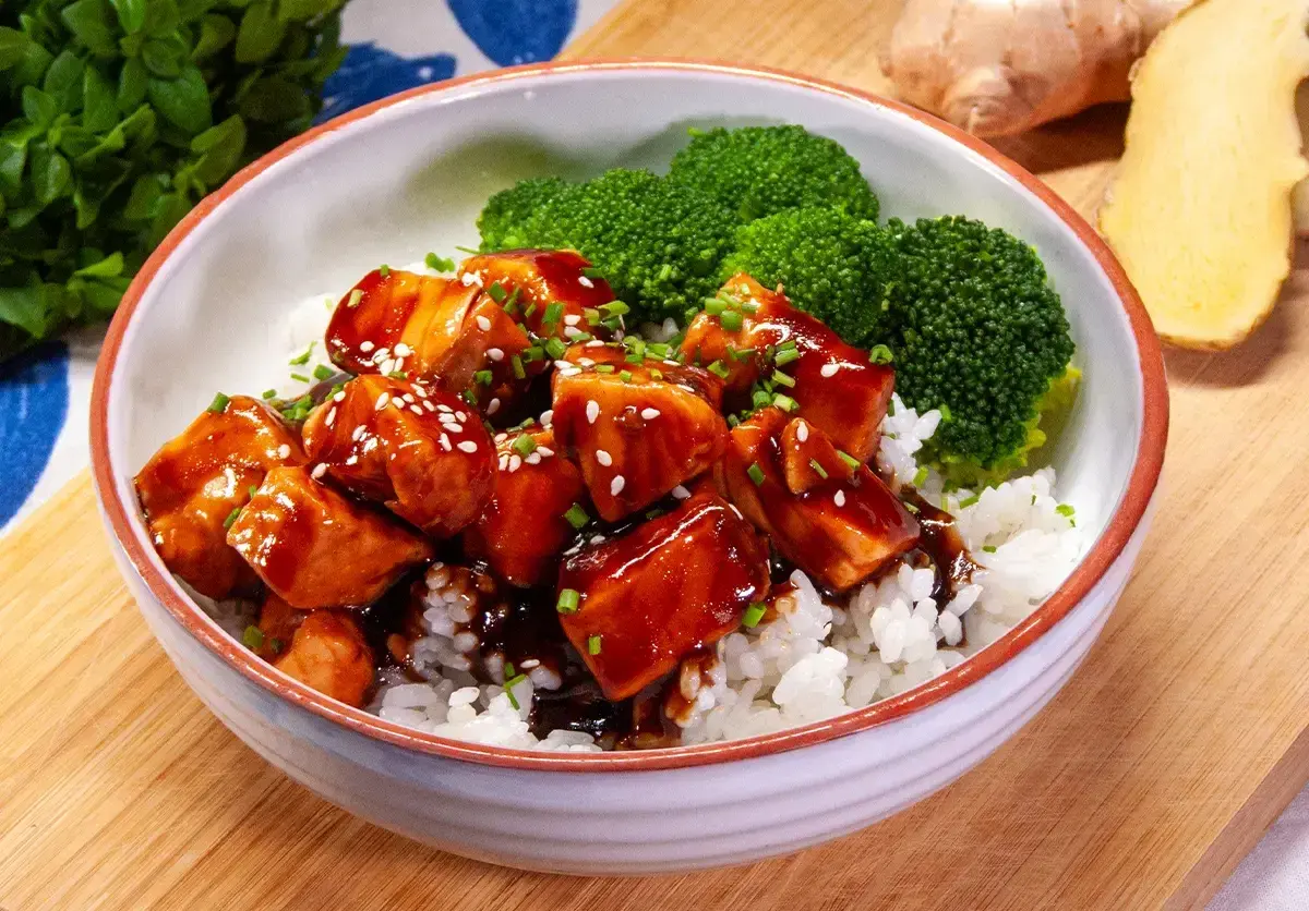 Aksamitny łosoś w sosie teriyaki, podany z ryżem i brokułami, posypany sezamem i szczypiorkiem. Pyszne danie gotowe do spożycia.