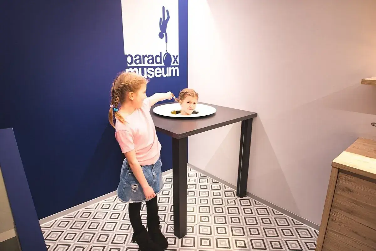 Flicka med flätor pekar på ett huvud som sticker upp ur ett bord på Paradox Museum.
