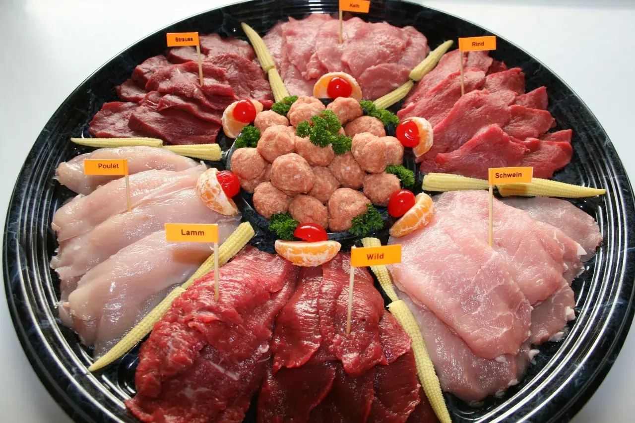 Plateau de viandes variées pour fondue : poulet, agneau, bœuf, porc, veau et gibier, décoré de mini-maïs et d'agrumes.