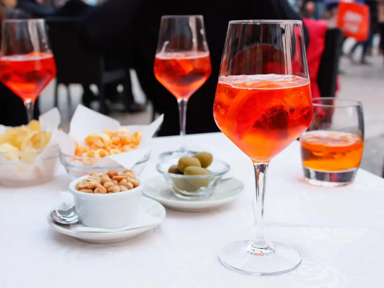 En aperitivo betyder njutning före maten. Här syns Aperol Spritz med snacks som nötter, oliver och chips.