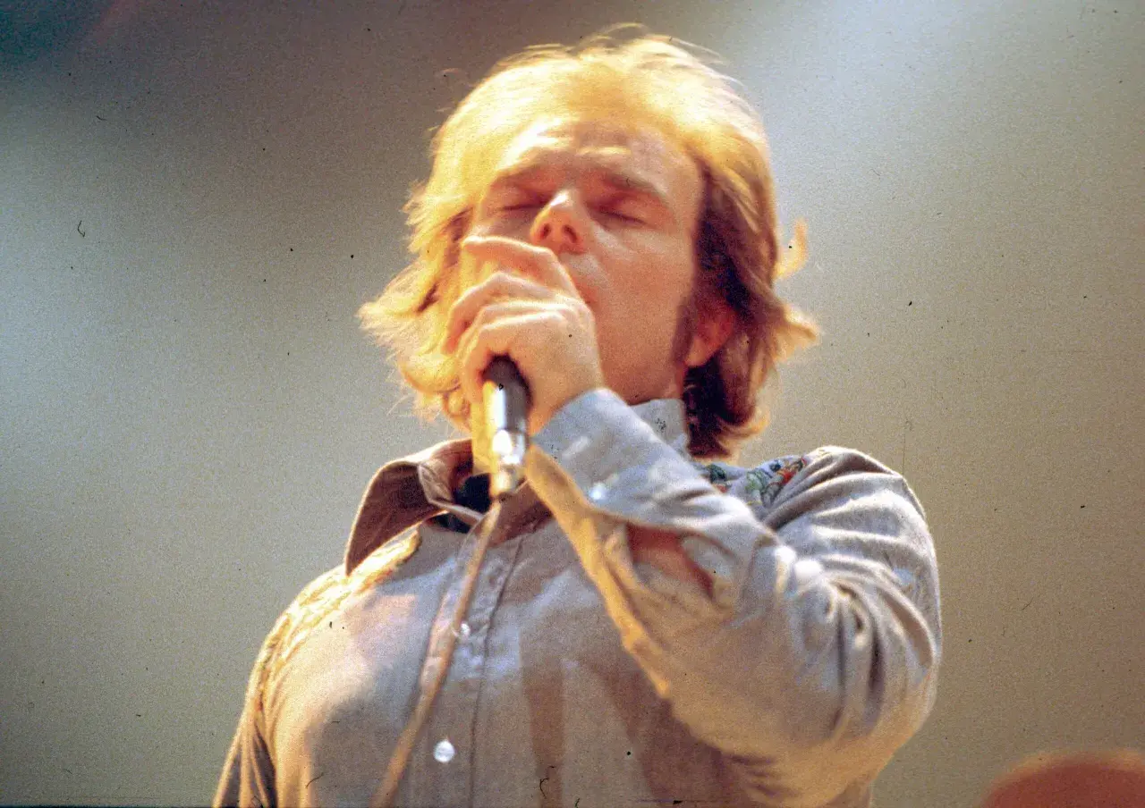 Van Morrison sings passionately into a microphone, his eyes closed. This image captures a moment from one of his legendary performances, perhaps hinting at the setlists that have defined his career.