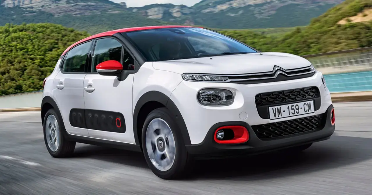 Biały Citroen C3 2025 z czerwonym dachem i lusterkami jedzie po drodze, otoczony zielonymi wzgórzami.