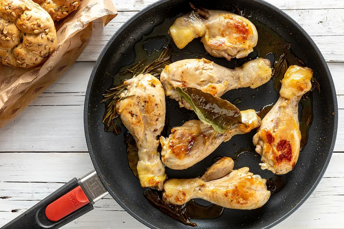 Cosce di pollo in padella, dorate e succulente, con rosmarino e alloro. Accompagnate da panini integrali.