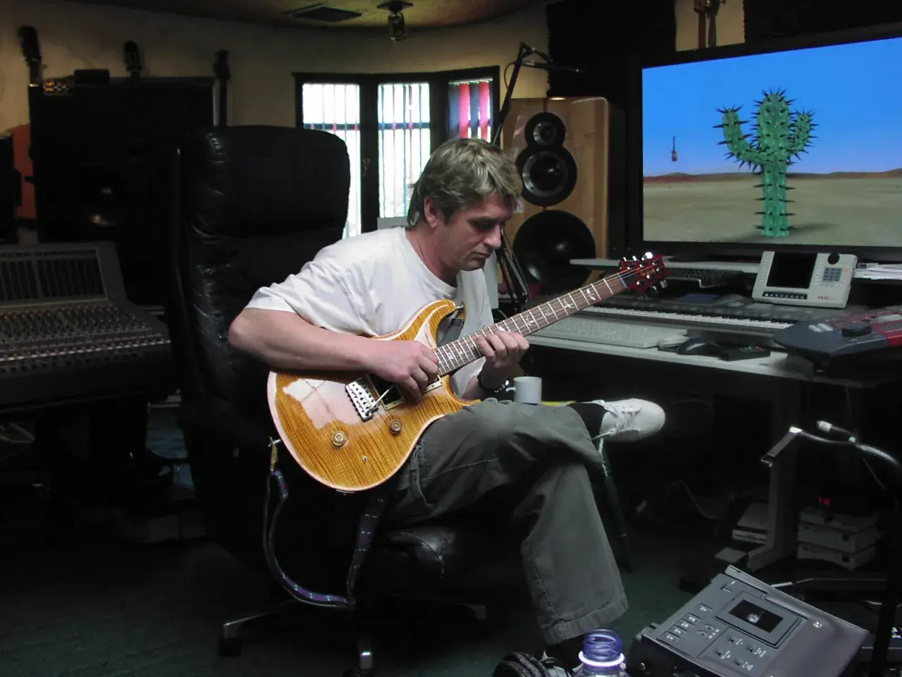 Mike Oldfield w studiu, gra na gitarze. Na ekranie komputerowym kaktus na pustyni, jak w jego utworach.