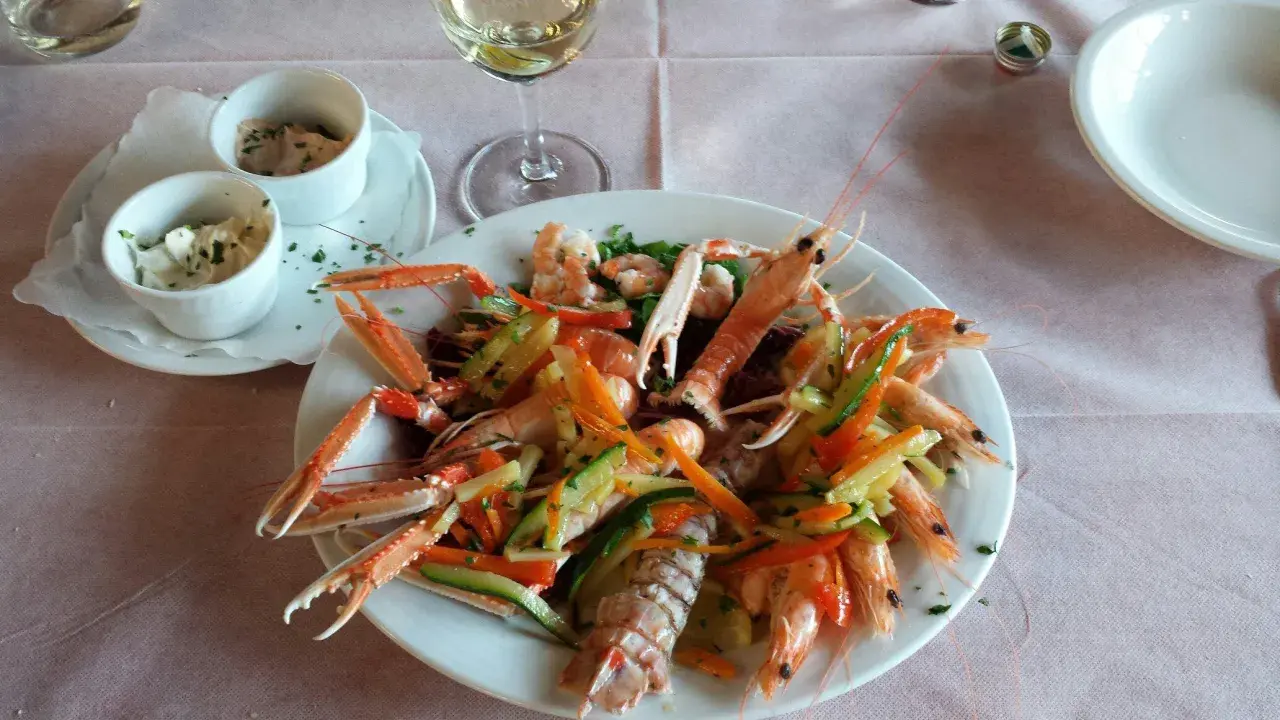 Un piatto di scampi e gamberi con verdure miste, un bicchiere di vino bianco e salse, un'ottima cena al conte Max Monte Roberto.