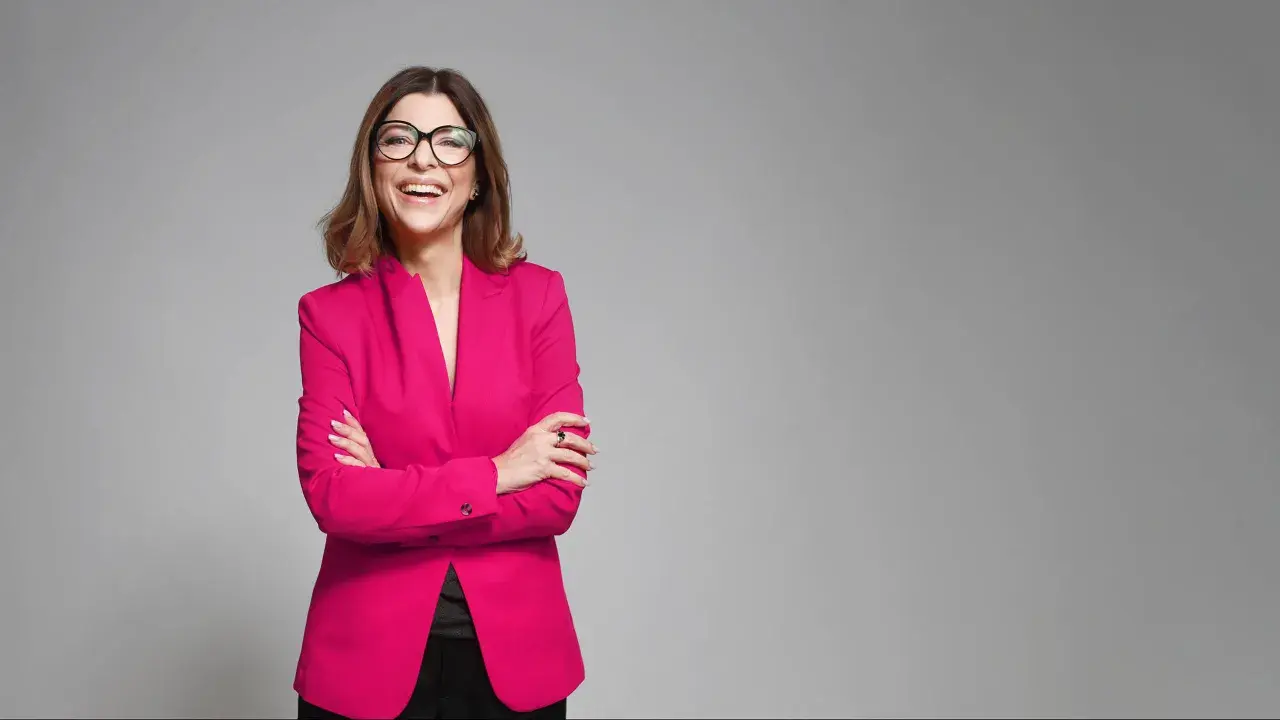 Uśmiechnięta kobieta w różowym żakiecie i okularach, prezentująca styl business formal.