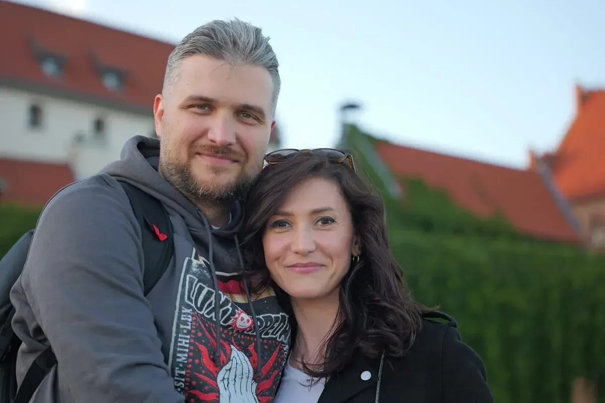 Ewa Zajączkowska-Hernik i jej mąż, uśmiechnięci na tle zabytkowych budynków.