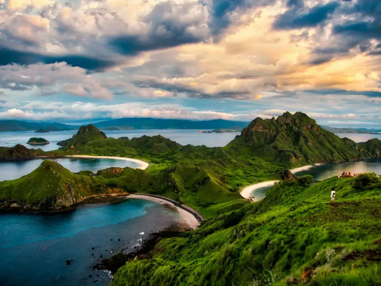 Grüne Hügel und weiße Sandstrände im Komodo Nationalpark, Indonesien. Ein einsamer Wanderer genießt die atemberaubende Aussicht auf das Meer.